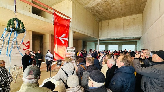 Viele Menschen feiern in der Halle des neuen Stadtteilzentrums Knieper das Richtfest. An der Decke hängt eine Richtkrone, vorne stehen Redner an einem Pult. © HANSESTADT Stralsund l Pressestelle Foto: HANSESTADT Stralsund l Pressestelle