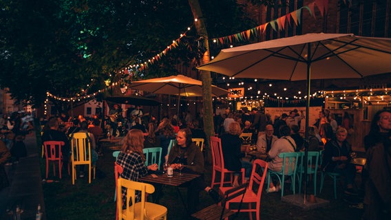 Viele Menschen sitzen auf bunten Stühlen im Pop-Up-Biergarten beim Stralsunder Sommergarten. © Michelle Dynio 