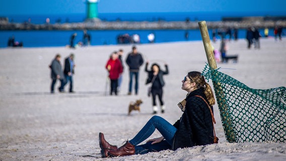 a young woman is sitting in the sand on a fence post on the beach in Warnemünde.  © dpa photo: Jens Büttner