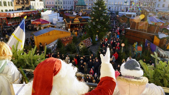 Ein Weihnachtsmann winkt vom Rathausbalkon zum Weihnachtsmarkt herunter. © NDR Foto: Christoph Woest