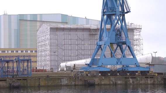 Großes Baugerüst vor dem Wismarer Werftgebäude. Davor steht ein blauer Kran. © NDR Foto: Christoph Woest