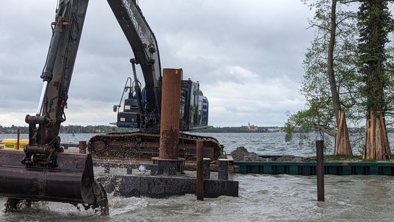 Ein Bagger auf einem Ponton, im Hintergrund der Schweriner See und das Schloss. © Christoph Loose Foto: Chris Loose