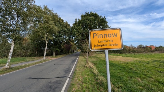 Das Ortsschild der Gemeinde Pinnow steht an einer Landstraße, im Hintergrund Bäume © Christoph Loose Foto: Chris Loose