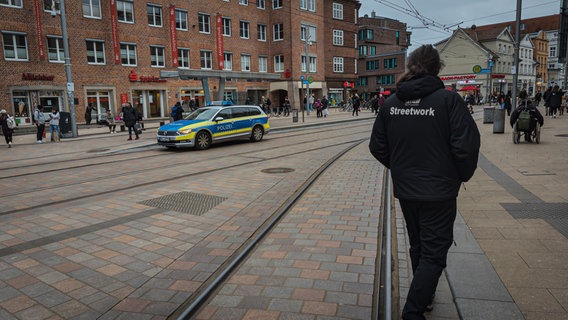 Ein Straßensozialarbeiter und ein Polizeiauto auf einem gefüllten Platz © Christoph Loose 