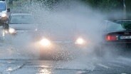 Regengischt spritzt auf der Straße vor einem Auto in die Luft. © dpa Foto: Stefan Sauer