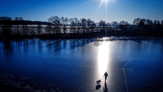 Ein Eisangler ist mit einem Schlitten auf dem zugefrorenen Vietlübber See unterwegs. © Jens Büttner/dpa 