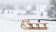 Ein Holzschlitten vor einer verschneiten Winterlandschaft im Büsenbachtal nahe Buchholz in der Nordheide. © Alexander Cornelius Mühlhausen 