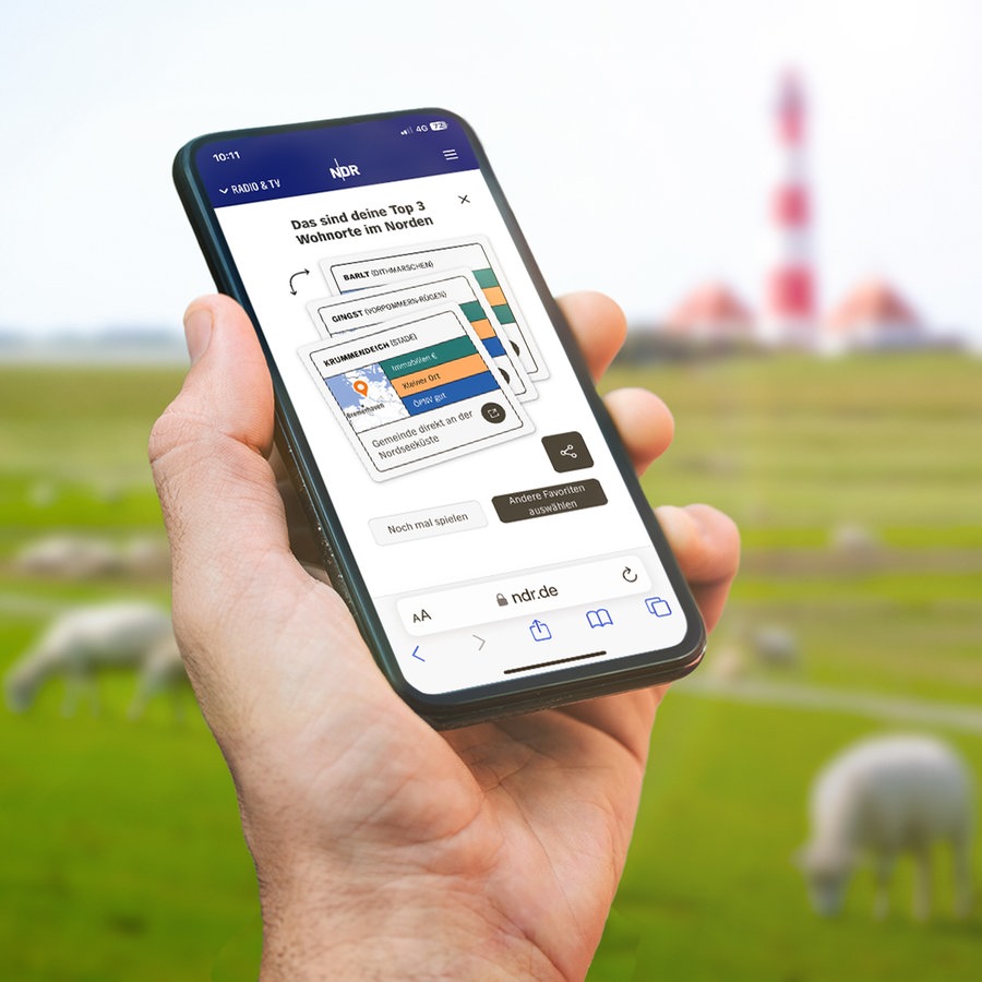 Eine Hand hält ein Smartphone mit dem News-Spiel "NDR Wohn-O-Mat" vor einer norddeutschen Landschaft mit Schafen und Leuchtturm © Fotolia.com Foto: JFL Photography