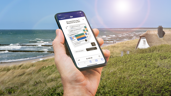 Eine Hand hält ein Smartphone mit dem News-Spiel "NDR Wohn-O-Mat" vor einer Düne und einem Reetdachhaus © Fotolia, PantherMedia Foto: dieter76, Peopleimages
