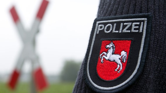 Ein Polizeiwappen auf einem Ärmel ist an einem unbeschrankten Bahnübergang mit Andreaskreuz zu sehen. © picture alliance / dpa | Friso Gentsch Foto: Friso Gentsch