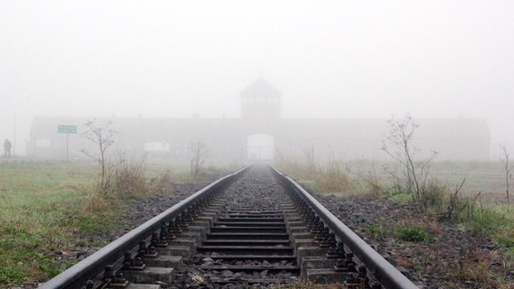 Vom Bahnhof Auschwitz kommend führt ein Gleis Richtung Torhaus vom KZ Auschwitz-Birkenau, Nebel verdeckt das Gebäude. © picture alliance / zb Foto: Frank Schumann