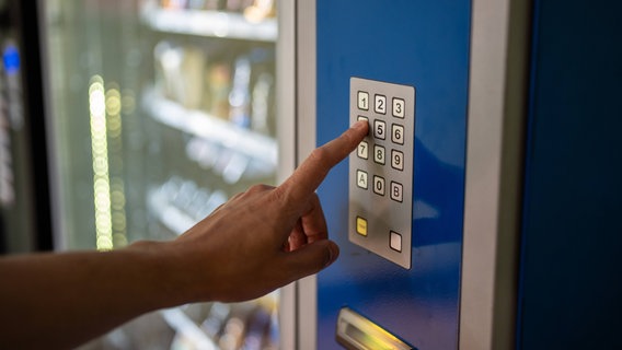 Eine Hand drückt einen Knopf an einen Automaten für Snacks. © IMAGO / Zoonar 