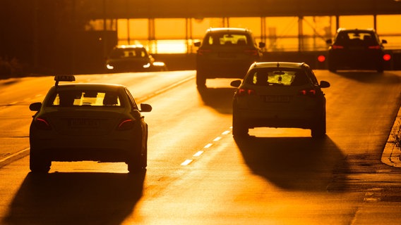 Autos fahren über eine Straße, die von der aufgehenden Sonne in warmes Licht getaucht wird. © picture alliance/dpa | Julian Stratenschulte Foto: picture alliance/dpa | Julian Stratenschulte