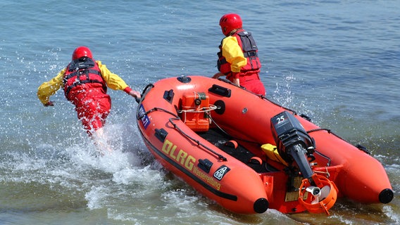 Zwei Personen der Deutschen Lebensrettungs-Gesellschaft (DLRG) rennen mit einem Rettungsboot ins Wasser. © DLRG 