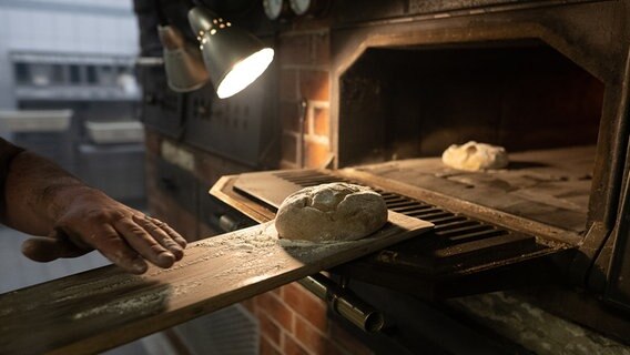 Ein Brot wird in einen Holzofen geschoben. © picture alliance/dpa | Swen Pförtner Foto: Swen Pförtner