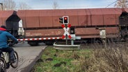 Ein Radfahrer wartet an einem geschlossenen Bahnübergang, während ein Güterzug durchfährt. © NDR Foto: Julia Scheper