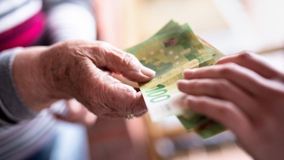 Eine junge Frau lässt sich von einer über 90-jährigen Frau mehrere hundert Euro an einer Haustür geben. © picture alliance/Matthias Balk Foto: Matthias Balk