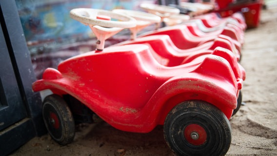 Mehrere Bobbycars stehen unter einem Vordach auf dem Spielplatz eines Kindergartens. © picture alliance/dpa | Christian Charisius Foto: Christian Charisius