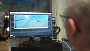 Ein Mann schaut auf einen Monitor auf dem Kameras zur automatisierten Überwachung in einem Schwimmbad angezeigt werden. © NDR 