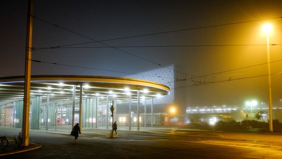 Zwei Menschen laufen bei Nebel und im Dunkeln vor einem großen Gebäude entlang. © picture alliance/dpa Foto: Stefan Jaitner