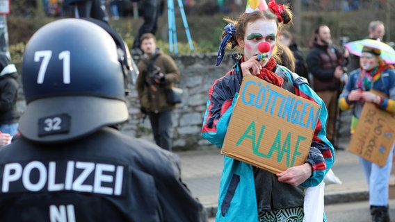 Eine als Clown verkleidete Demonstrantin steht einem Polizisten bei der Gegendemonstrantion zu einer Versammlung von Anhängern der Querdenker-Szene gegenüber. © dpa Foto: Stefan Rampfel