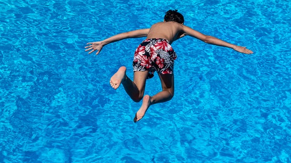 Ein Junge springt in einem Freibad vom Drei-Meter-Turm ins Wasser. © dpa-Bildfunk Foto: Swen Pförtner