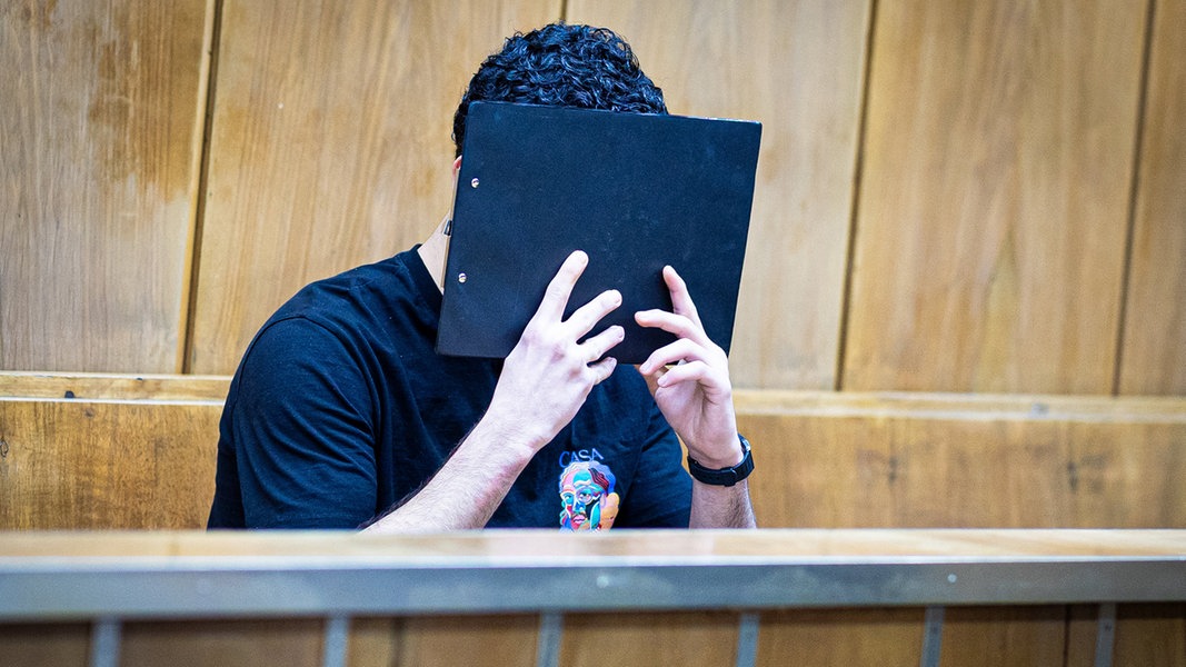 Der Angeklagte verdeckt sein Gesicht mit einer Mappe bei Prozessauftakt in einem Saal im Landgericht Hannover. 