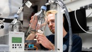 Ein Mann hält eine Flasche mit extrahiertem Wasser in der Hand. © picture alliance/dpa Foto: Michael Matthey