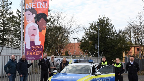 In Celle stehen Polizisten am Orange Day vor einer Flagge, die sich gegen Gewalt an Frauen wendet. © Polizeiinspektion Celle 