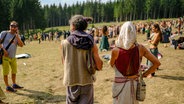 Ein Mann und eine Frau in alternativer Kleidung gucken auf eine Versammlung von Hippies im Harz. © Landkreis Goslar 