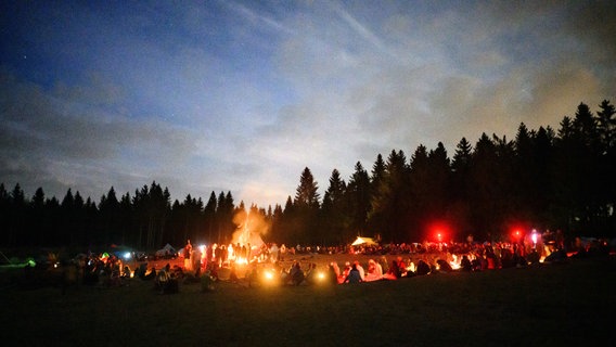 Bad Grund: Hunderte Teilnehmer sitzen bei einem Zeltlager in einem großen Kreis rund um ein Lagerfeuer und essen das gemeinsam zubereitete Abendessen. © dpa-Bildfunk Foto: Julian Stratenschulte