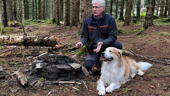 Michael Rudolph, Niedersächsische Landesforsten, sitzt im Wald neben einem Hund und gibt ein Interview zru "Rainbow Family". © NDR Foto: Max von Schwartz