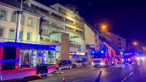 Mehrere Feuerwehrfahrzeuge stehen vor einem Mehrfamilienhaus in Braunschweig, der Leiterwagen hat seine Leiter ausgefahren und ein Feuerwehrmann klettert hoch. © Feuerwehr Braunschweig Foto: Feuerwehr Braunschweig