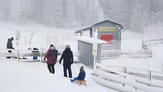 Menschen spazieren auf dem verschneiten Wurmberg, ein Kind wird auf einem Schlitten gezogen. © dpa Foto: Matthias Bein