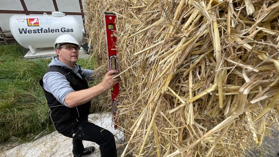 Ein Mann kontrolliert mit einer Wasserwaage, ob Strohballen senkrecht übereinander liegen. © NDR Foto: Jan Fragel