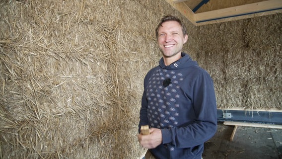 Der Architekt Florian Hoppe steht vor einer Wand aus Strohballen. © NDR 