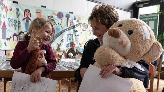Jasmin Kaatz (r), Sprecherin der Polizeiinspektion Göttingen, sitzt mit ihrem Teddybär "Kitty" und einem Kind der Kindertagesstätte Weende-Nord beim Teddybär-Krankenhaus am Uniklinikum Göttingen. © Swen Pförtner/dpa Foto: Swen Pförtner