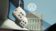 Das Volkswagen Logo ist durch die Frontscheibe eines Pkw zu sehen, an der Stoffwürfel hängen. © dpa Foto: Julian Stratenschulte