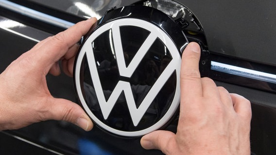 Ein Mitarbeiter von Volkswagen das VW-Logo in die Front eines Autos ein. © picture alliance/dpa Foto: Hendrik Schmidt