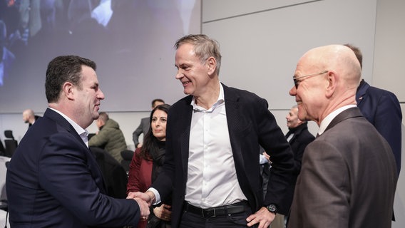 Arbeits- und Sozialminister Hubertus Heil (l) und der Vorstandsvorsitzende des deutschen Automobilherstellers Volkswagen (VW), Oliver Blume, schütteln sich die Hände, während die Vorsitzende des Gesamt- und Konzernbetriebsrats des Volkswagen-Konzerns, Daniela Cavallo (hinten, 2. v. l), vor einer unternehmensweiten Versammlung im Stammwerk des Unternehmens in Wolfsburg zusieht. © Ronny Hartmann/AFP POOL/dpa Foto: Ronny Hartmann