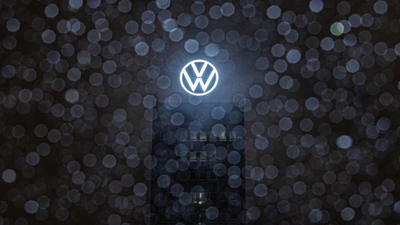 Das Logo auf dem Dach des VW-Markenhochhauses leuchtet am frühen Morgen bei Regenwetter in Wolfsburg. ©  Moritz Frankenberg/dpa Foto: Moritz Frankenberg/dpa