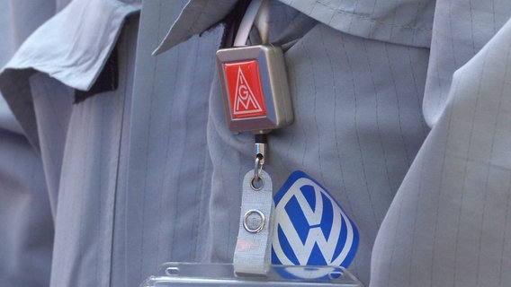 Ein IG Metall-Emblem und ein VW-Emblem hängen am Arbeitsanzugs eines VW-Mitarbeiters in Wolfsburg. © picture alliance/dpa Foto: Dominique Leppin