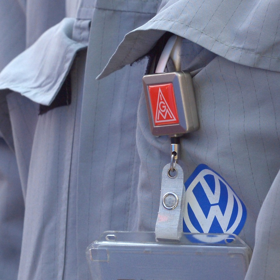 Ein IG Metall-Emblem und ein VW-Emblem hängen am Arbeitsanzugs eines VW-Mitarbeiters in Wolfsburg. © picture alliance/dpa Foto: Dominique Leppin