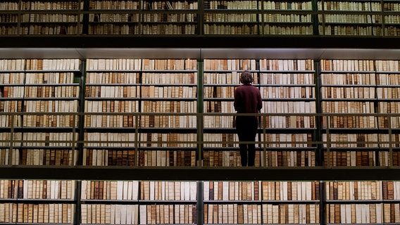 Eine Mitarbeiterin steht vor Büchern in der Herzog-August-Bibliothek in Wolfenbüttel. © picture alliance / dpa | Julian Stratenschulte Foto: Julian Stratenschulte