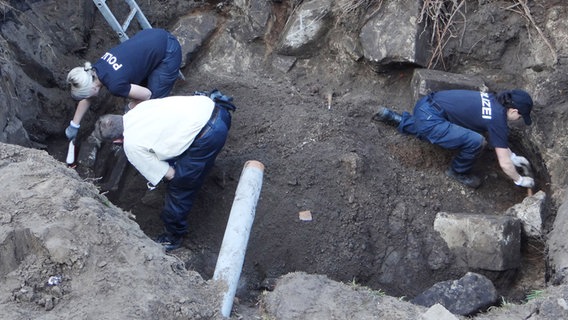Das Polizeibild zeigt Beamte, die nach Beweisstücken graben. © Polizei Lüneburg/dpa 