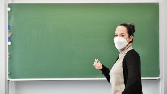 Eine Lehrerin steht mit einer Maske an einer Tafel. © Picture Alliance Foto: Frank May