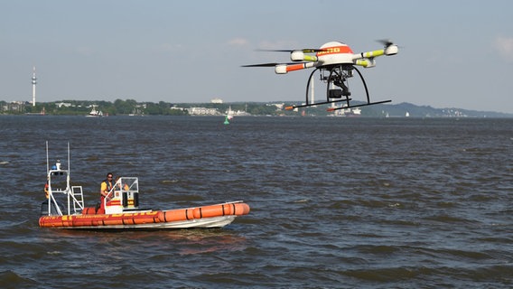 Eine Drohne der Deutschen Lebens-Rettungs-Gesellschaft (DLRG) fliegt, mit einer Wärmebildkamera ausgestattet, zu Übungszwecken über die Elbe, im Hintergrund ein Rettungsboot. © dpa Foto: Carmen Jaspersen