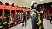 Zwei Feuerwehrmänner ziehen sich in einem Umkleideraum ihre Einsatzkleidung an. © NDR Foto: Julius Matuschik