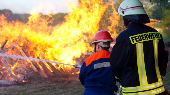 Ein Mitglied der freiwilligen Feuerwehr löscht gemeinsam mit einem Nachwuchsmitglied ein großes Lagerfeuer. © dpa - picture alliance Foto: Patrick Pleul
