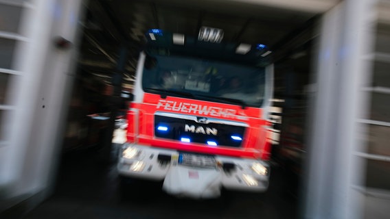 Ein Feuerwehrfahrzeug in Unschärfe fährt aus dem Hallentor einer Feuerwache. © NDR Foto: Julius Matuschik